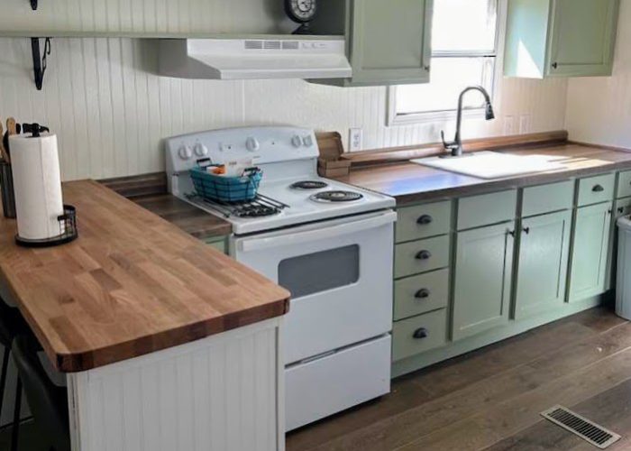 Farmhouse-style kitchen with sage green cabinets, white appliances, and butcher block counters.