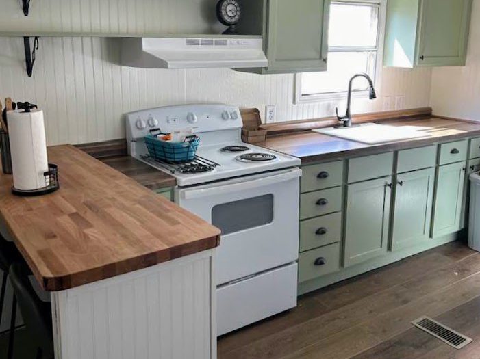 Farmhouse-style kitchen with sage green cabinets, white appliances, and butcher block counters.