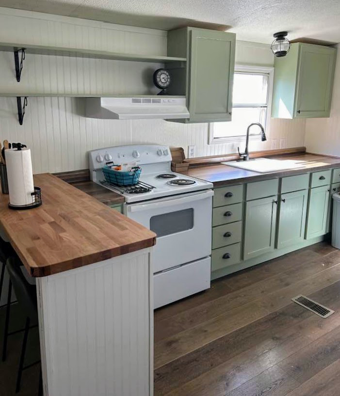 Farmhouse-style kitchen with sage green cabinets, white appliances, and butcher block counters.