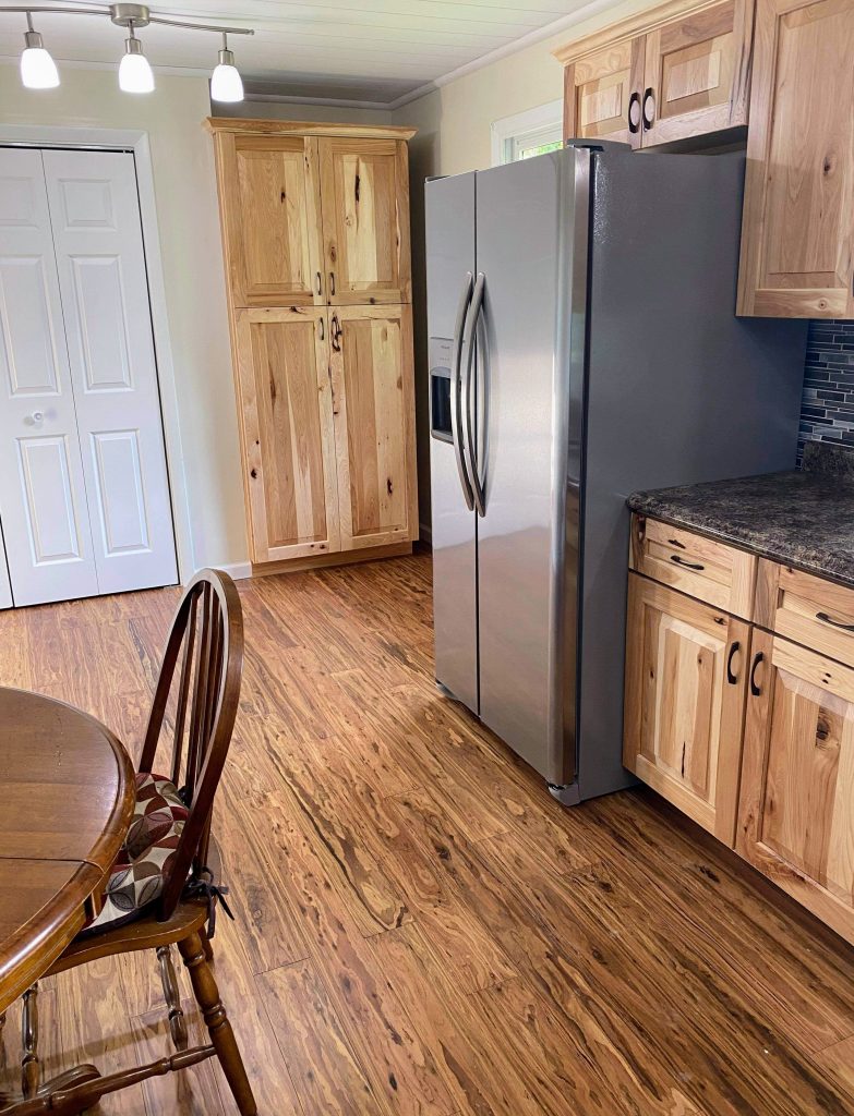 Modern kitchen with natural wood cabinets, stainless steel refrigerator, wood-look flooring, and a round wooden dining table