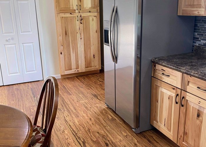 Modern kitchen with natural wood cabinets, stainless steel refrigerator, wood-look flooring, and a round wooden dining table