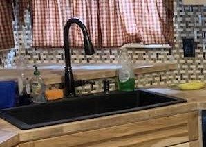 Rustic kitchen with natural wood cabinets and drawers, a matte black sink and faucet, and a mosaic tile backsplash.