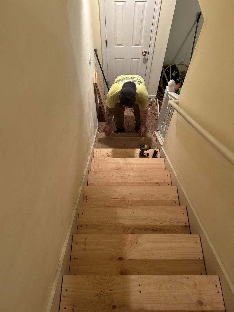 Contractor installing raw wood stair treads in an indoor staircase during a home renovation project.
