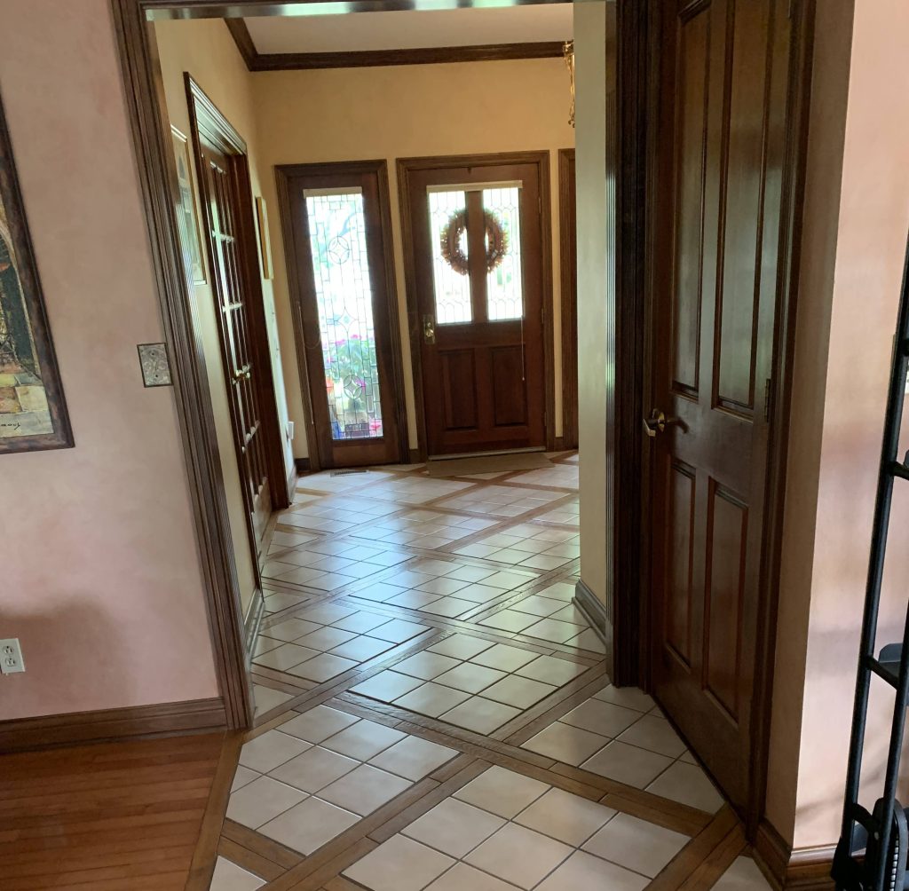 Traditional front entryway with decorative tile flooring, wood trim, and a solid wood door with stained glass sidelights.