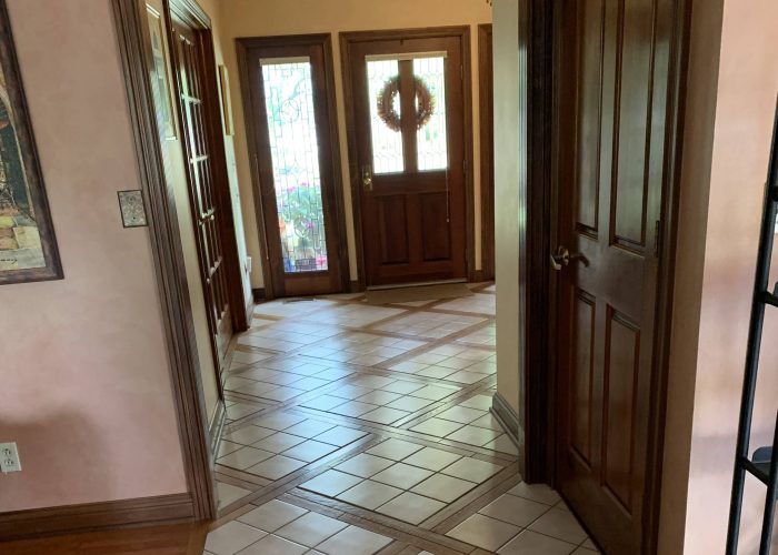 Traditional front entryway with decorative tile flooring, wood trim, and a solid wood door with stained glass sidelights.