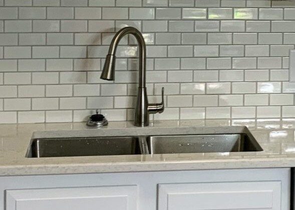 Modern kitchen with white shaker-style cabinets, a double stainless steel sink, brushed nickel faucet, and glossy white subway tile backsplash.